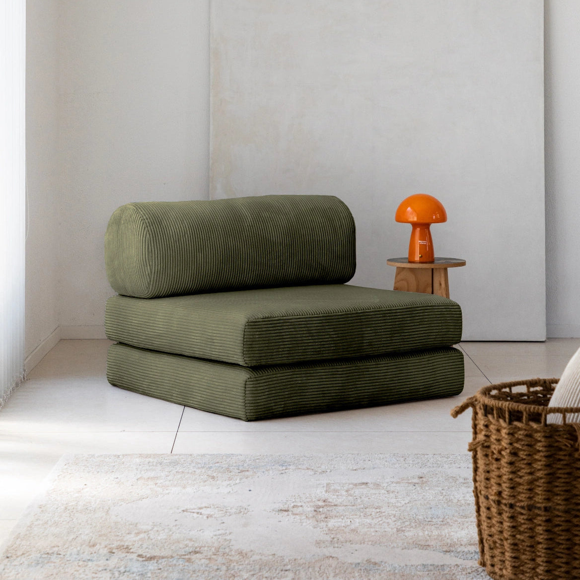 Green cushioned chair in a minimalistic room with a white wall and wooden floor.